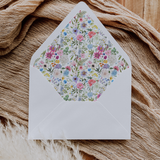 A flat lay of elegant wedding invitation envelopes, partially open to reveal beautifully designed envelope liners in various styles, including floral, modern, and classic patterns. The envelope inserts add a touch of luxury and sophistication to the stationery set.